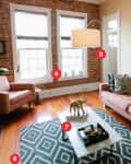 Living room with pink sofas, geometric rug, large plant, brick walls, and abstract painting.
