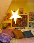 Cozy bedroom with star-shaped light, colorful pillows, and eclectic wall art on a yellow wall.