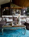 Brown sectional sofa with patterned pillows, mirrored coffee table, candles, and a large plant in a cozy living room.