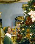 Two people dressed as elves decorating a Christmas tree in a toy store.