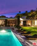 Modern house with illuminated pool, outdoor seating, and lush garden at sunset.