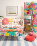 Colorful polka dot sofa with matching ottoman, pink cushions, potted plant, and abstract room divider in a vibrant living room.