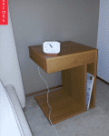 Wooden bedside table with a drawer, clock on top, and magazine stored below.