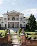 Grand villa with neoclassical architecture, manicured gardens, statues, and a gated entrance.
