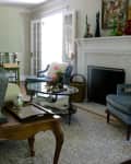 Living room with blue armchairs, white sofa, ornate lamps, glass coffee table, and decorative fireplace mantel.