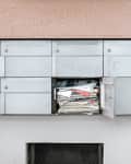 Row of gray mailboxes with one open, overflowing with letters and magazines.