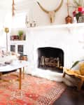 Eclectic living room with a tufted sofa, colorful pillows, white fireplace, and a vibrant patterned rug.