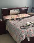 Cluttered bedroom with a dark wood bed, floral bedding, and a nightstand with scattered items.