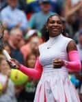 Tennis player in a white and pink outfit holding a racket, smiling on the court with a crowd in the background.