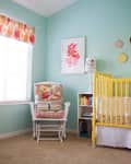Nursery with yellow crib, floral rocking chair, pastel walls, and colorful wall art.