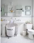 White bathroom with dual pedestal sinks, wire towel basket, wall-mounted mirrors, and decorative deer head.