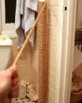 DIY cat scratching post wrapped in rope, placed in a tiled bathroom corner.