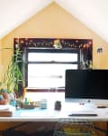 Home office with a large monitor, potted plants, string lights, and a clipboard on a yellow wall.