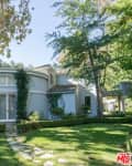 Circular house with large windows, surrounded by trees and manicured lawn, under a clear blue sky.