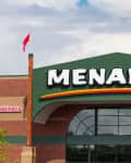 Menards store entrance with green and red signage, brick facade, and two red flags.