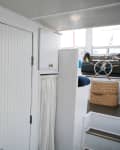 Nautical-themed room with a brass porthole mirror, wicker basket, and ship's wheel on a white paneled wall.