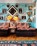 Eclectic living room with patterned sofas, vibrant wall art, and unique lamps on a wooden floor.