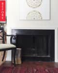 Fireplace with black frame, decorative art above, wooden chair, and red patterned rug.