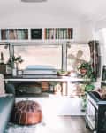 Cozy camper interior with a blue sofa, decorative pillows, bookshelves, plants, and a small fireplace.