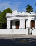 White colonial-style house with columns, arched windows, and palm trees in front.