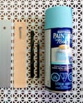 Retro blue phone, metal bracket, wood piece, screws, drill bits, and blue spray paint on patterned surface.