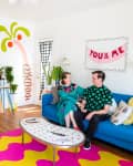 Colorful living room with a blue sofa, vibrant wall art, plants, and a couple sitting together.