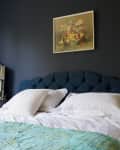 A bed with a navy headboard in front of a black wall.