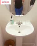 Pedestal sink with a round mirror, soap dispenser, and wicker basket in a small bathroom.