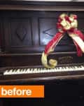 Antique upright piano with a red and gold ribbon bow on top.