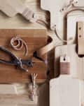 Wooden cutting boards with leather straps, hole punch tool, and screws on a light wood surface.