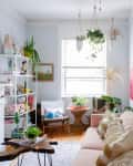 Living room with pink sofa, yellow door, hanging plants, and colorful decor on shelves.