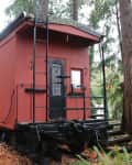 Red train caboose converted into a cabin, surrounded by lush forest trees and ferns.