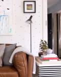 Brown leather sofa with patterned cushions, abstract painting, floor lamp, and books on a striped side table.