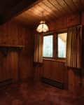 Wood-paneled room with two curtained windows, a wall shelf, and a hanging light fixture.