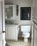 Small bathroom with white cabinets, toilet, wall mirror, and framed map art above the toilet.