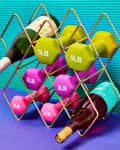 Wine rack holding colorful dumbbells and wine bottles on a purple surface with a teal background.