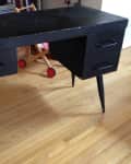 Worn black wooden desk with two drawers on each side, set on a light wood floor.