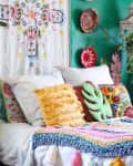 Bohemian bedroom with green walls, colorful pillows, plants, and woven wall decor.