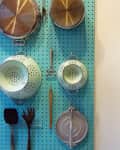 Kitchen pegboard with hanging colanders, pots, spatula, and utensils.