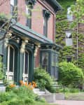 Historic brick townhouses with ivy-covered walls and lush gardens along a tree-lined sidewalk.