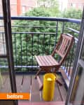 Small balcony with a wooden chair and a yellow trash can, overlooking green trees and brick buildings.