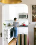 Woman cooking in a modern kitchen with marble countertops, white cabinets, and a red kettle on the stove.