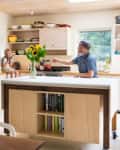Family in a bright kitchen with a child on the counter, sunflowers on the island, and a fridge covered in photos.