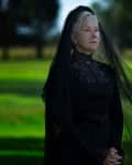 Elderly woman in black lace dress and veil standing in a green field.