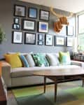 Living room with a beige sofa, colorful cushions, wooden coffee table, and a gallery wall with framed art and a moose head.