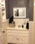 Small bathroom with white vanity, mirror, and gray walls, featuring a basket with towels and a soap dispenser.