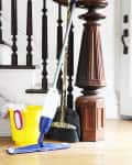 Mop, broom, and yellow bucket with cleaning supplies on wooden floor by staircase.