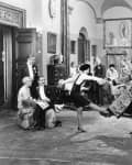 Elegant 1920s party scene with a couple dancing in a lavish room, surrounded by seated and standing guests.