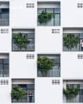 Modern apartment building facade with balconies, plants, and two people standing on separate balconies.