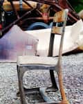 Rusty metal chair on gravel with old machinery in the background.
